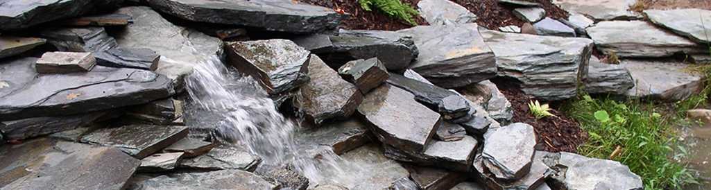 A slate rock waterfall in a garden surrounded by rocks.